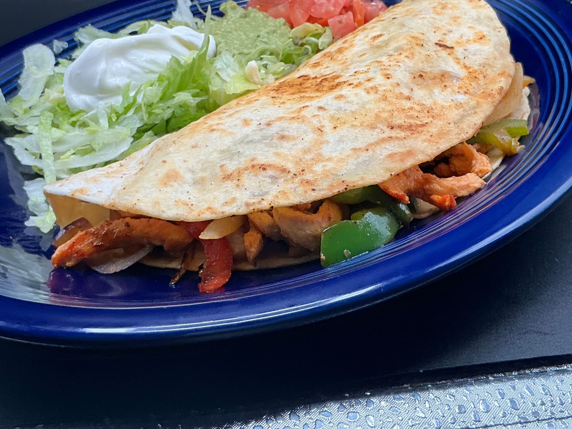 Fajita wrap on a blue plate with lettuce, sour cream, guacamole, and diced tomatoes.