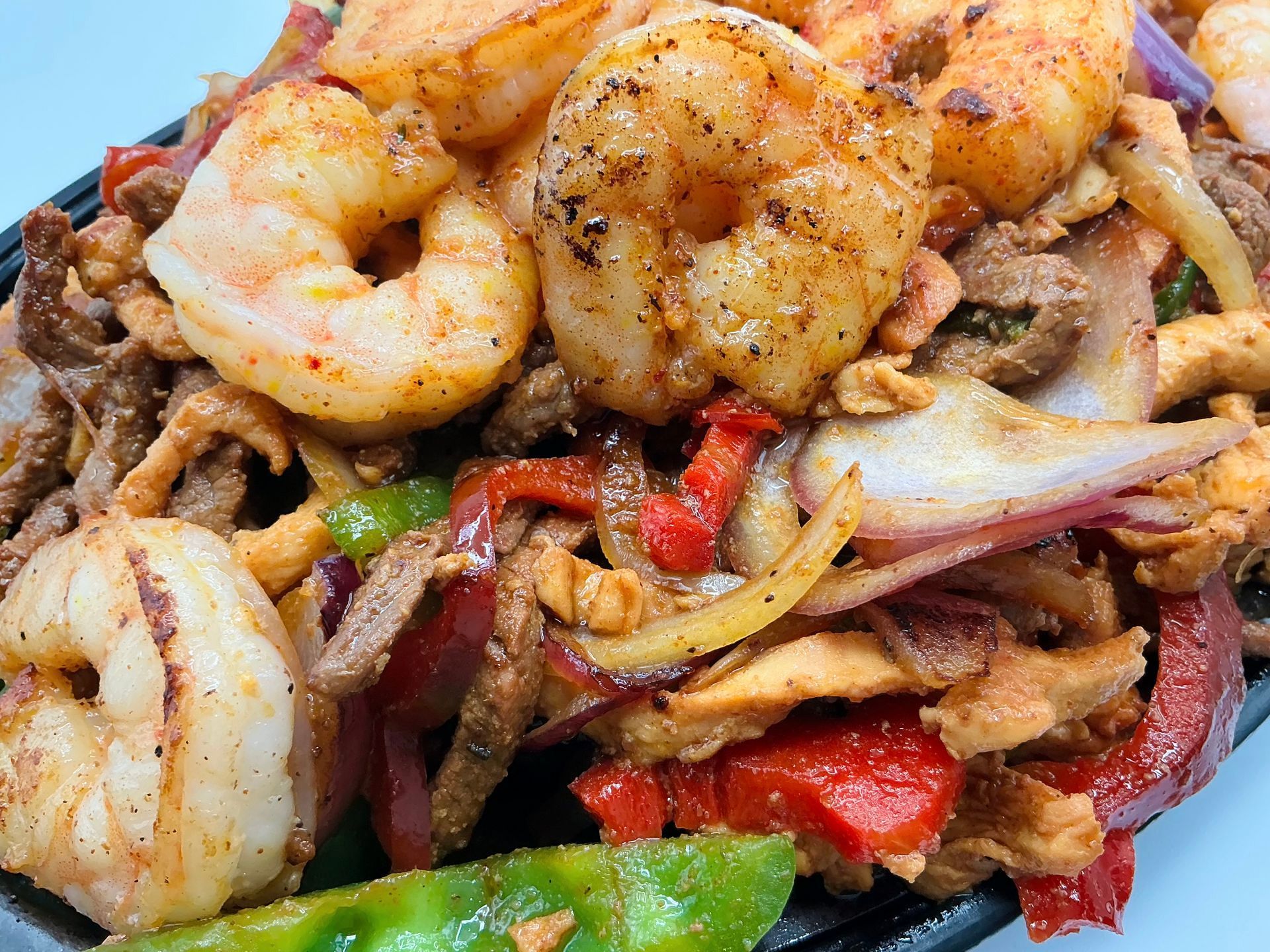 Close-up of a sizzling plate of shrimp, steak, chicken, red onions, and bell peppers.