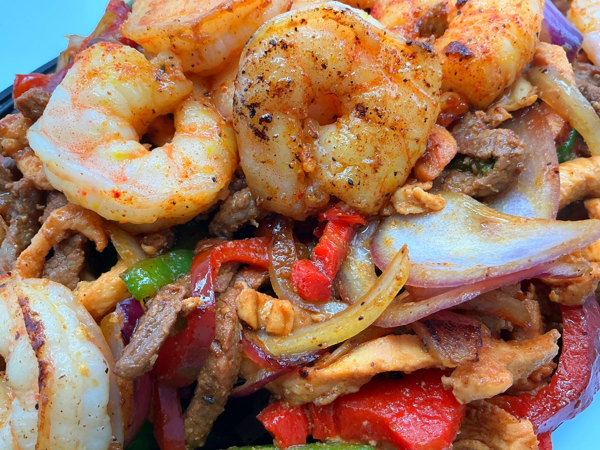Shrimp, steak, and chicken fajitas with peppers and onions.