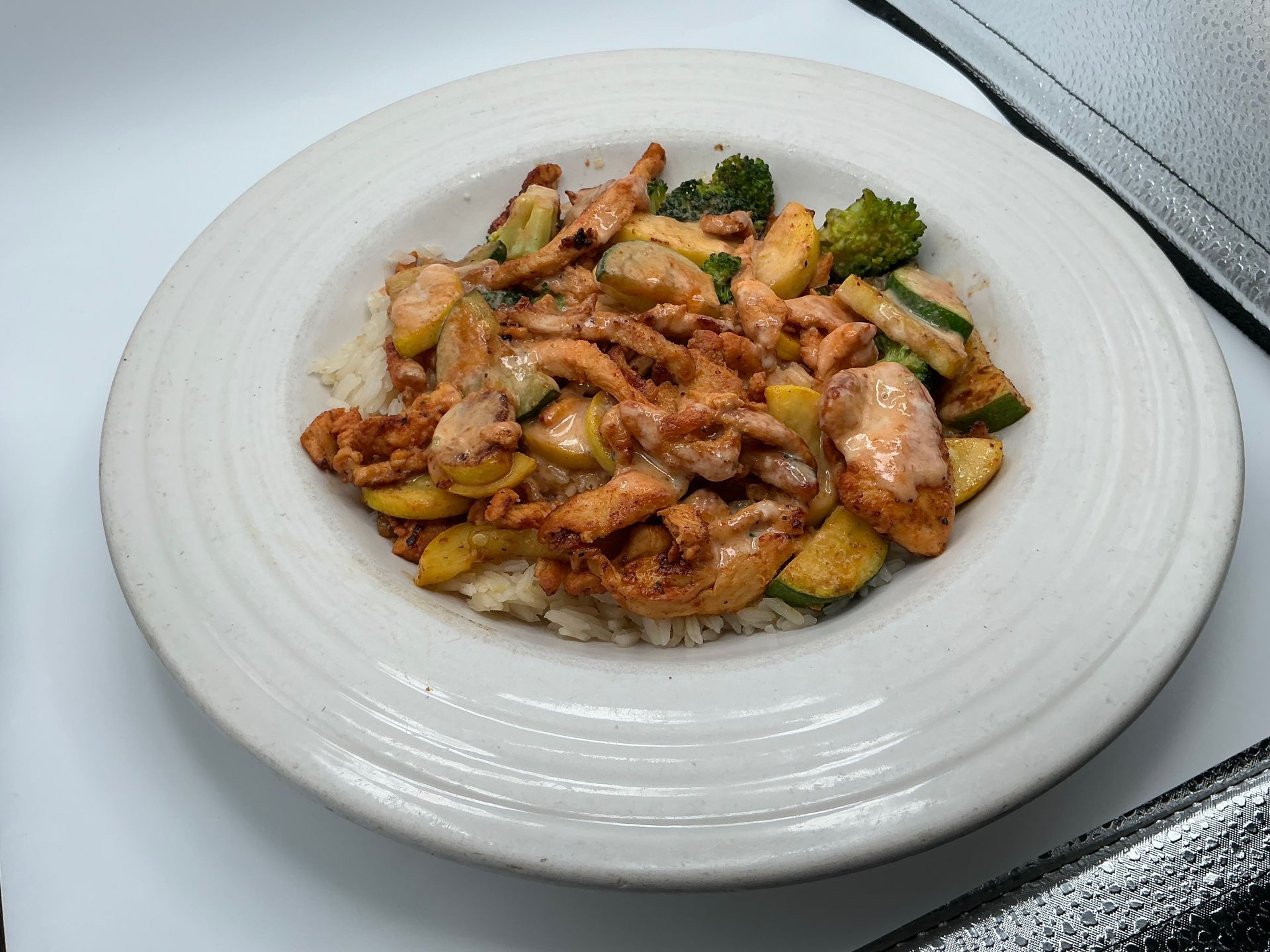 Chicken and vegetables over rice in a white bowl.