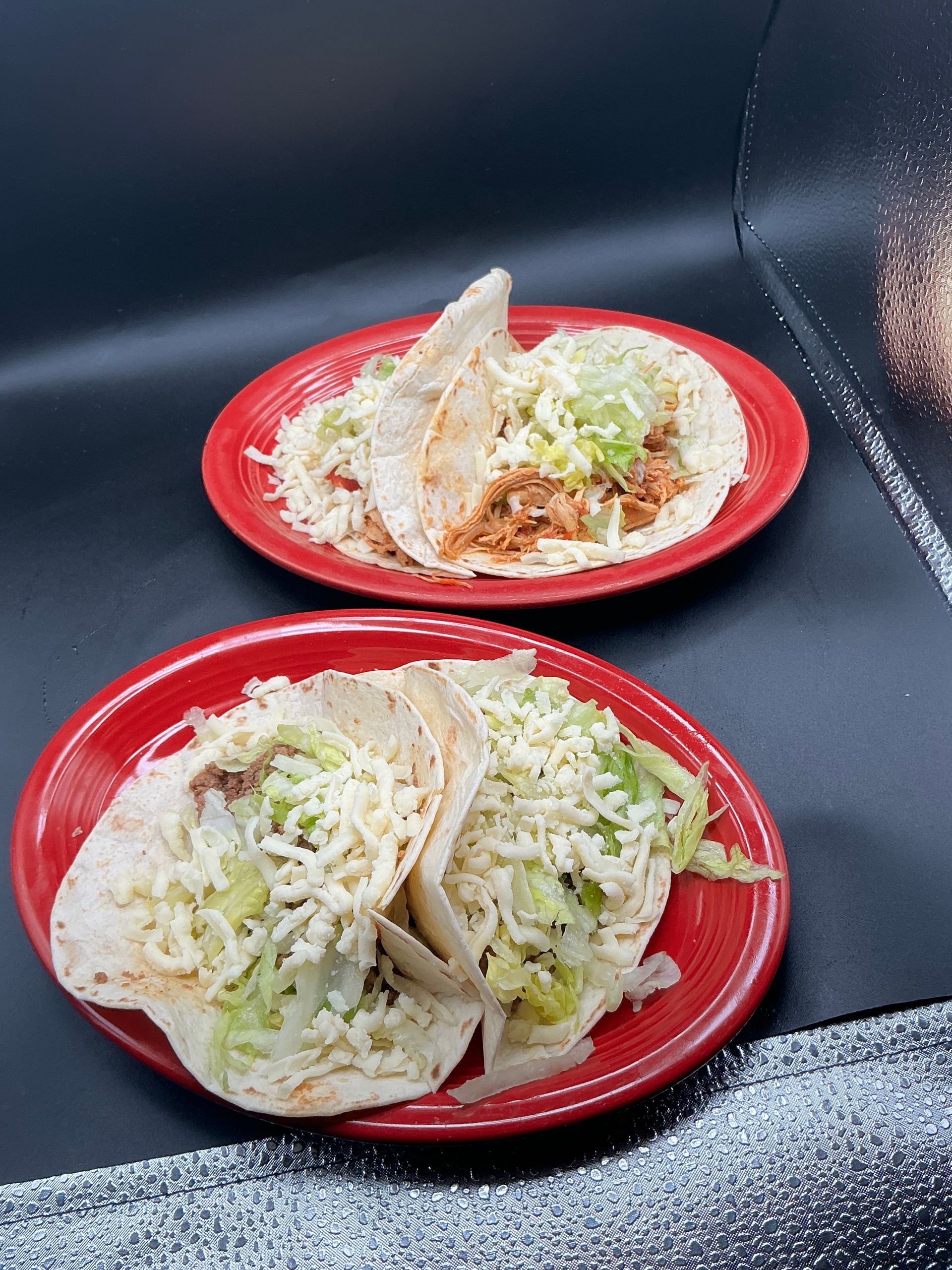 Two red plates with tacos topped with shredded lettuce and cheese.
