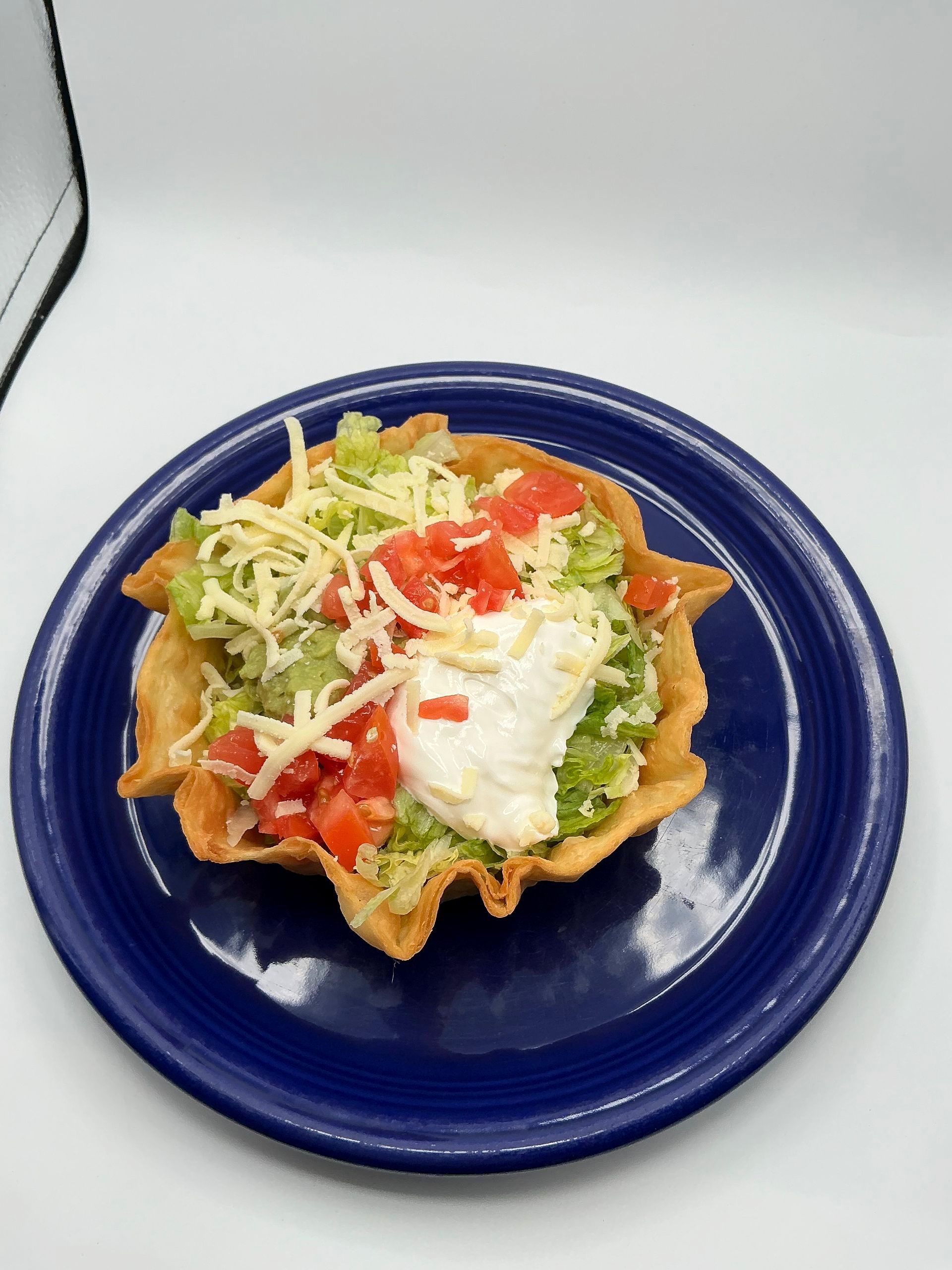 Taco salad in a crispy shell on a blue plate; contains shredded lettuce, tomato, cheese, and sour cream.