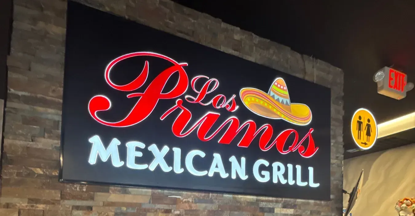 Sign for Los Primos Mexican Grill. Red and white lettering with sombrero graphic on a black background.