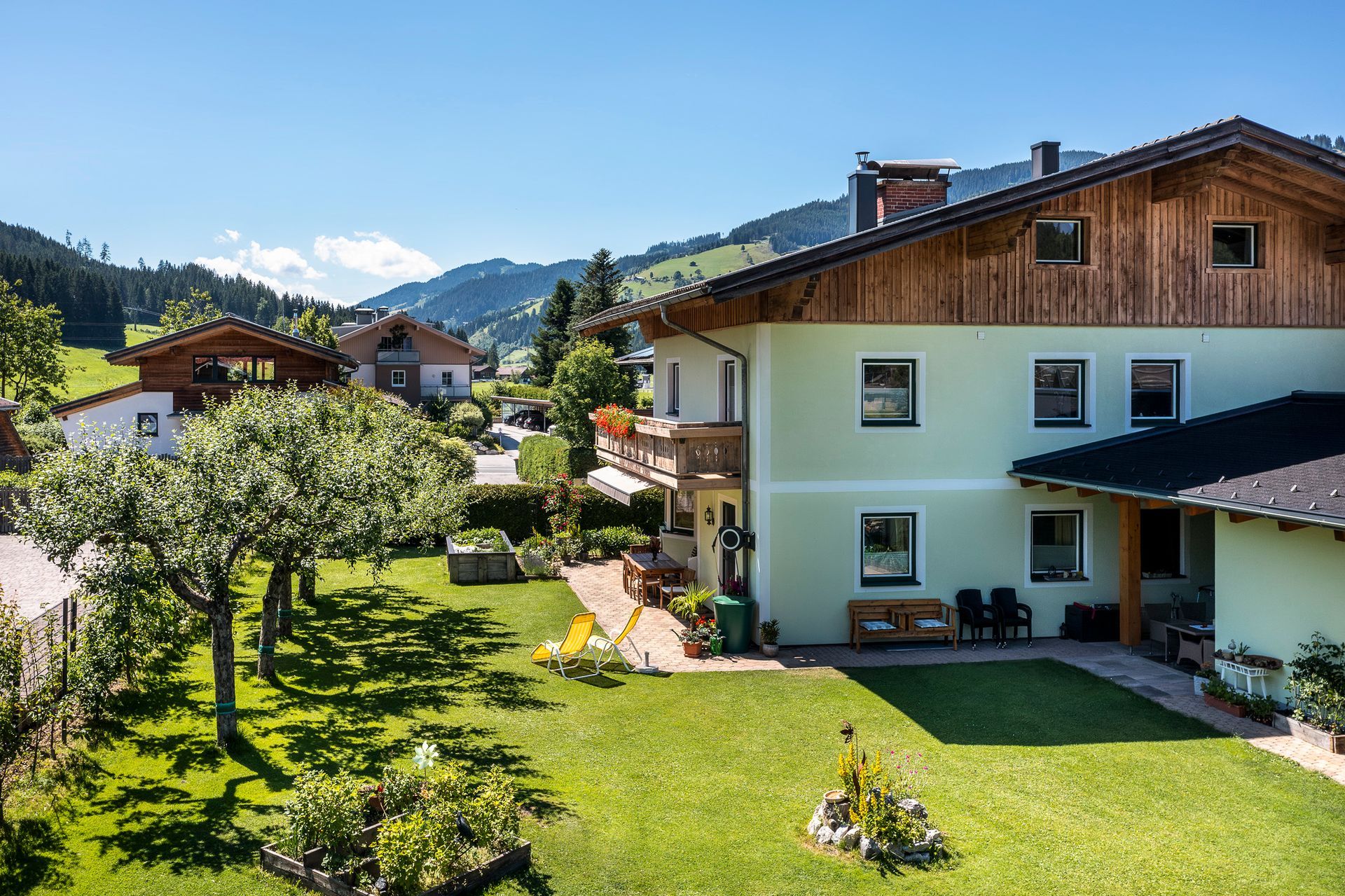 Sonniges Alpendorf mit Häusern, grünen Rasenflächen und Bergen im Hintergrund