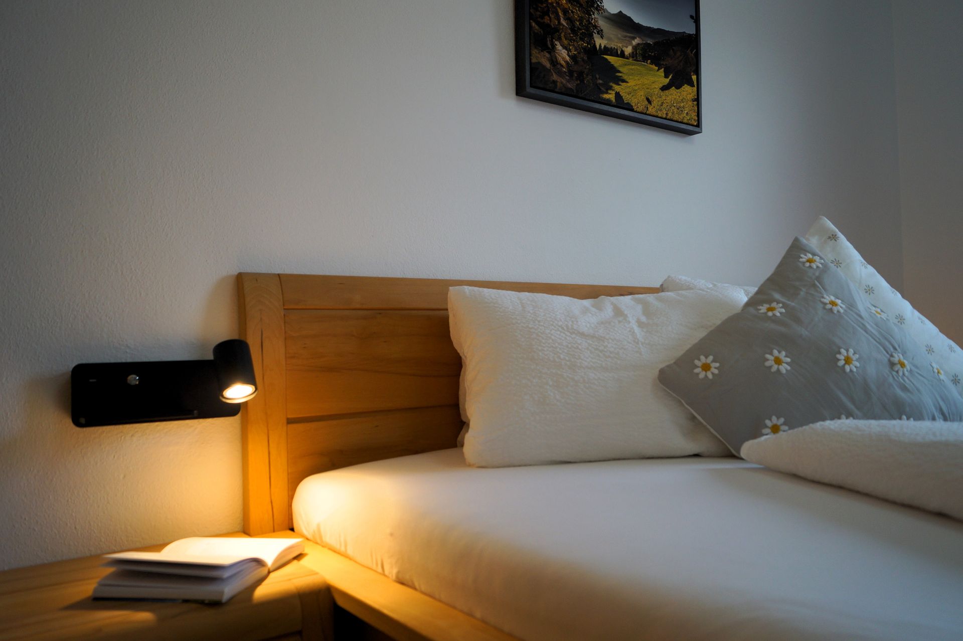 Gemütliches Schlafzimmer mit Holzbett, weißer Bettwäsche, Nachttischlampe und gerahmtem Wandbild