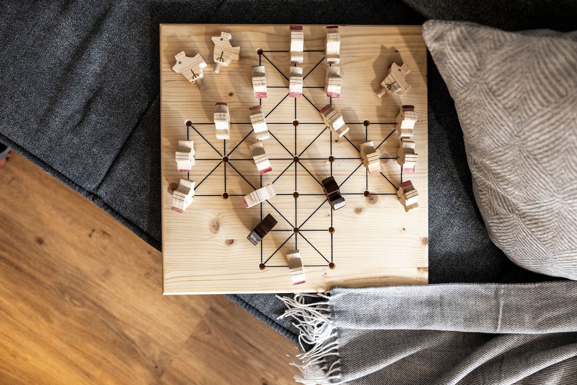 Ein hölzernes Spielbrett mit verstreuten Spielsteinen auf einem mit einer Decke bedeckten Sofa.