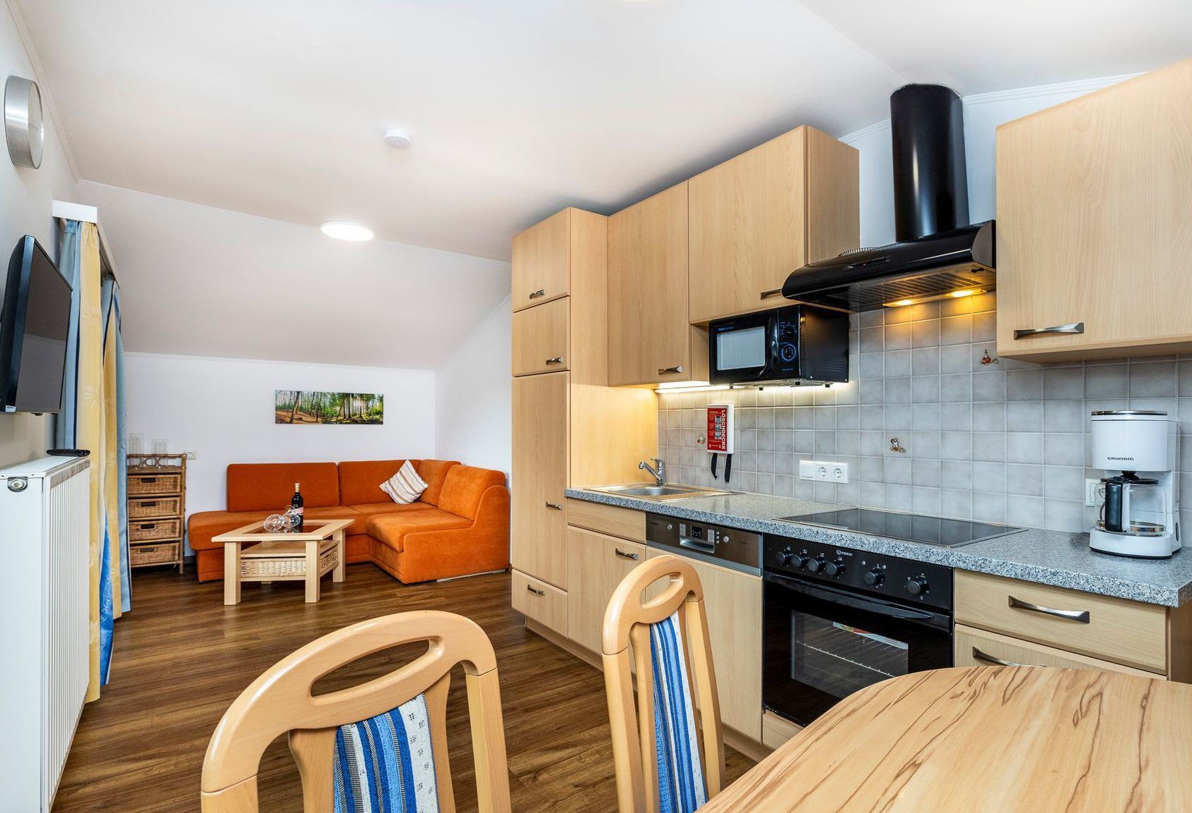 Moderne Küche und Essbereich mit hellen Holzschränken, Granitarbeitsplatten und einem orangefarbenen Sofa im Hintergrund