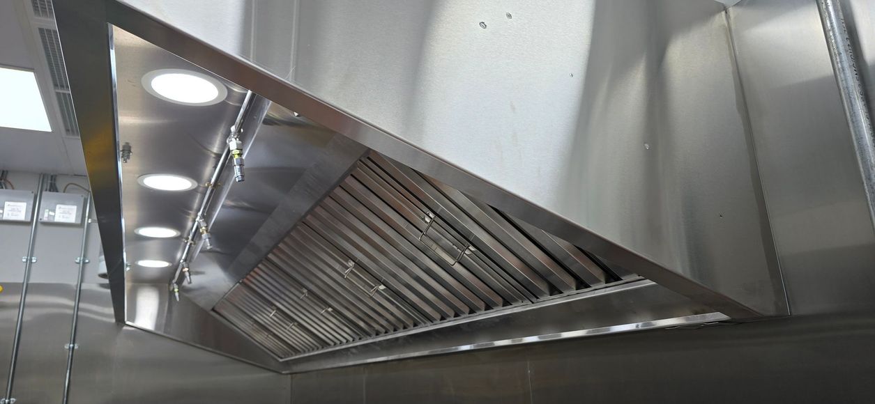 Stainless steel commercial kitchen range hood with lights and grease filters above a cooking area