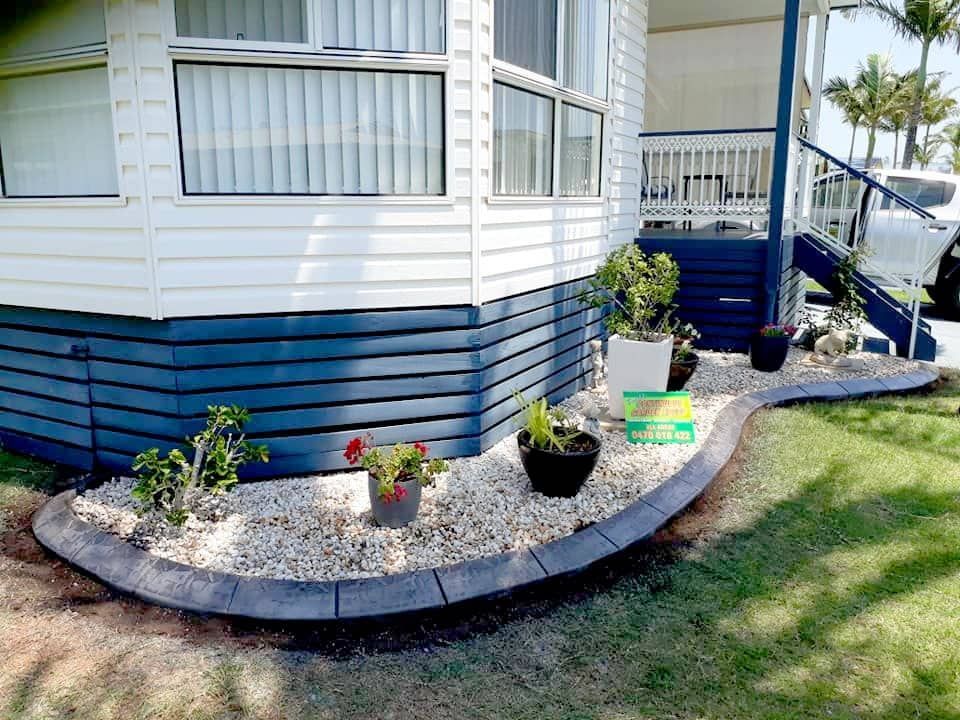 A Neatly Landscaped Garden Borders a White and Blue House — Brett's Continuous Garden Edges In Lakewood, NSW