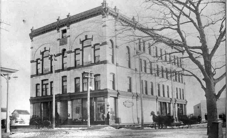 A black and white photo of a large building with a horse drawn carriage in front of it.
