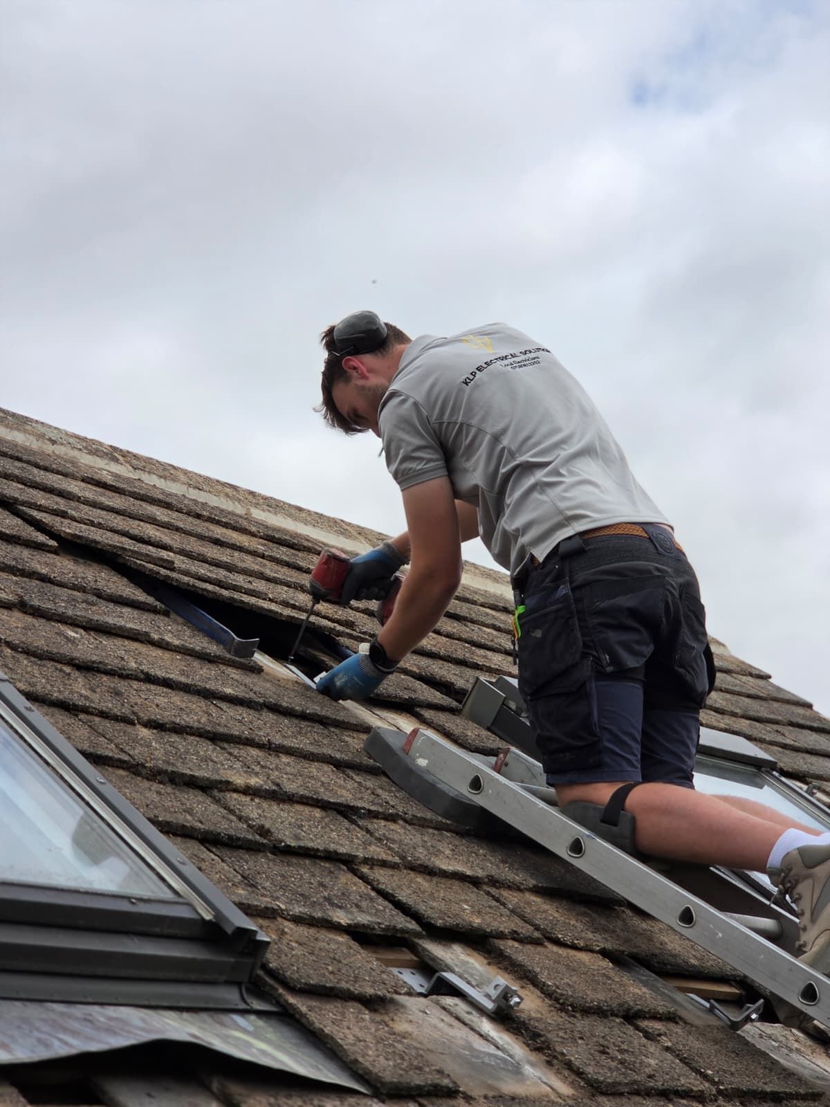 Man on a ladder cleaning a large slanted glass panel with a power tool outdoors