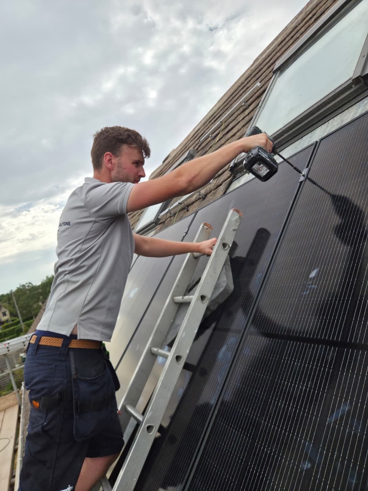 Man working on solar panels with a ladder on the side of a building