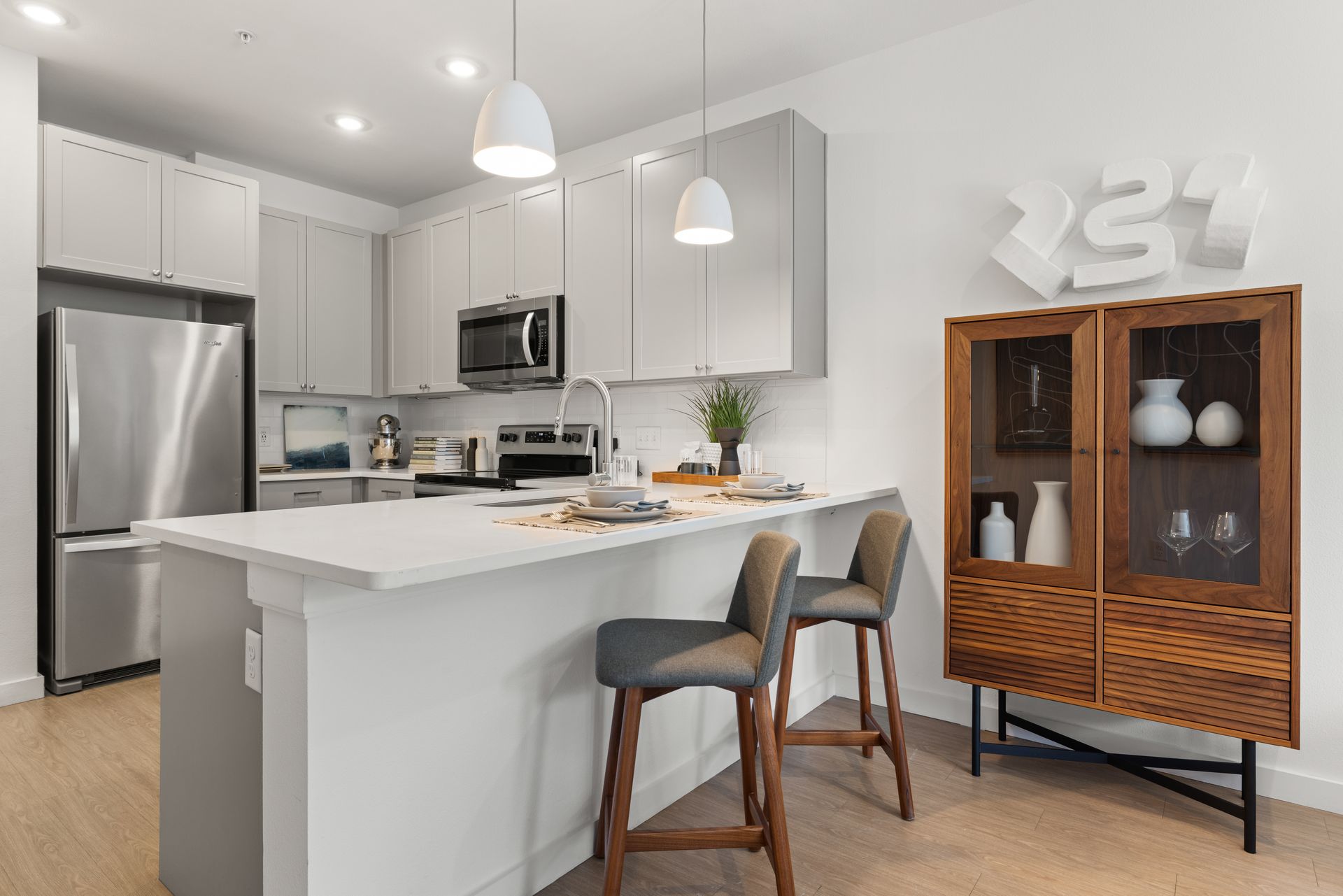 Modern kitchen interior with white cabinetry, stainless steel appliances, and a central island with bar stools. The back wall is accented with a teal color. There's a wooden display cabinet with glassware on the right and a dining area partially visible in the background at 44 South in Austin, TX.