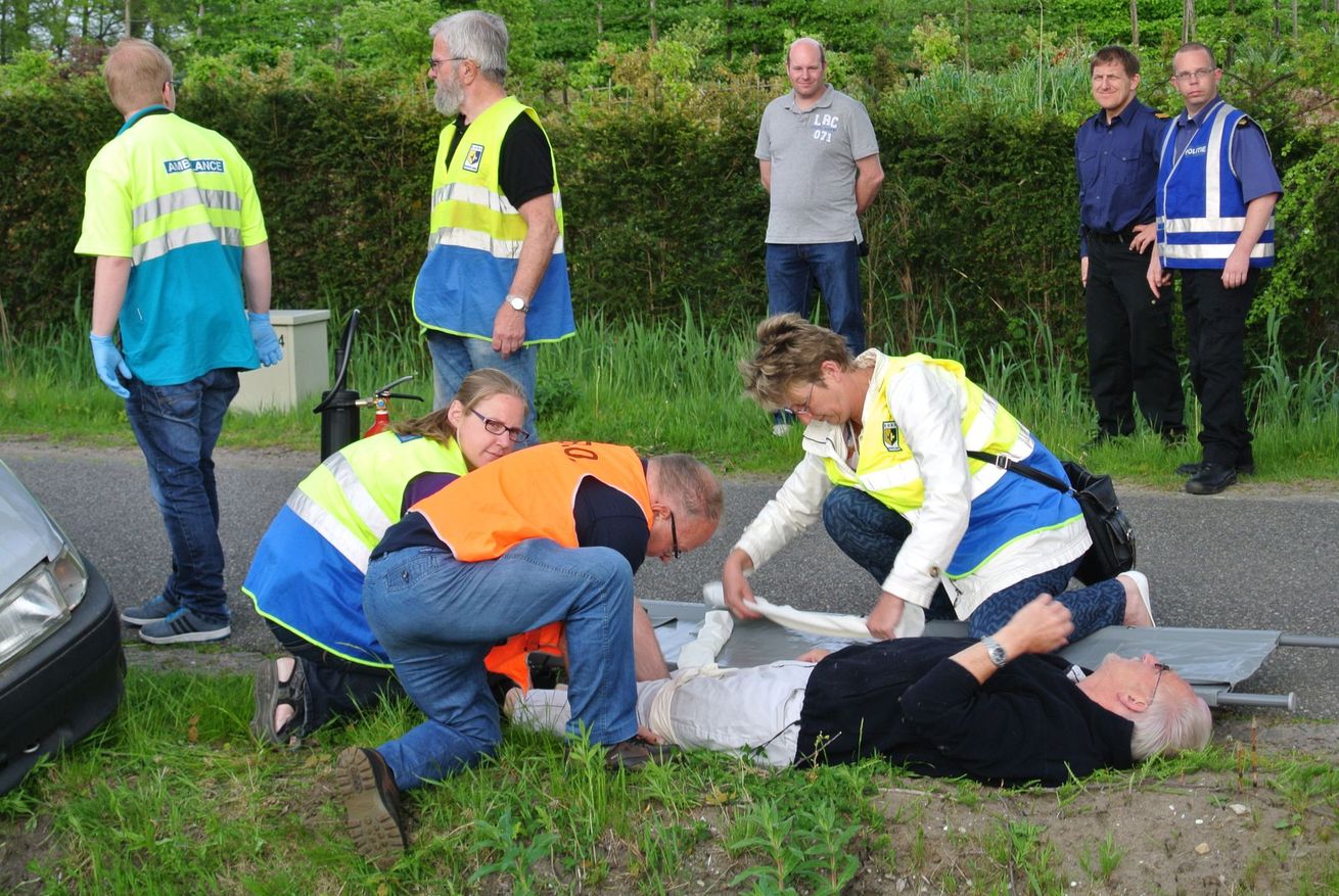 Hulpverleners verlenen eerste hulp aan een gewonde persoon die in het gras langs de weg ligt.