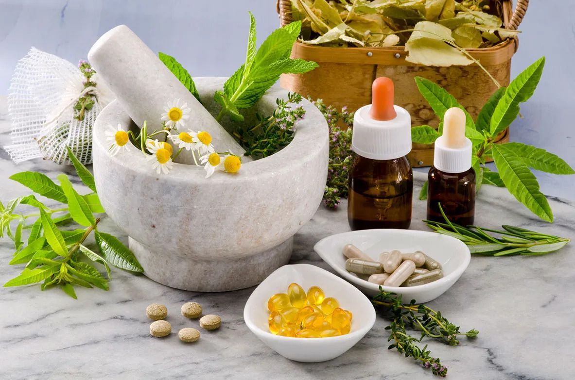 A mortar and pestle surrounded by herbs and pills on a table.