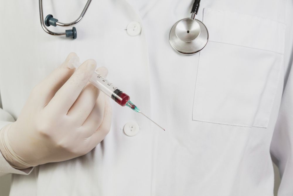 A doctor with a stethoscope around his neck is holding a syringe.