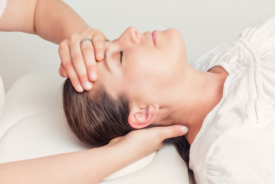 A woman is laying on a table getting a head massage.