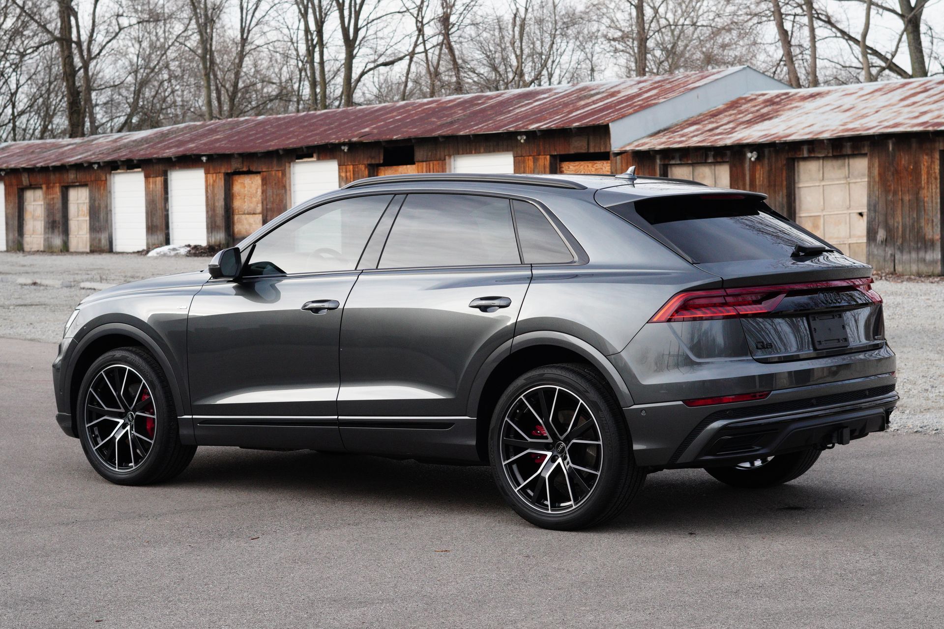 Dark gray Audi Q8 SUV parked in front of a rustic building. Black wheels with red brake calipers.