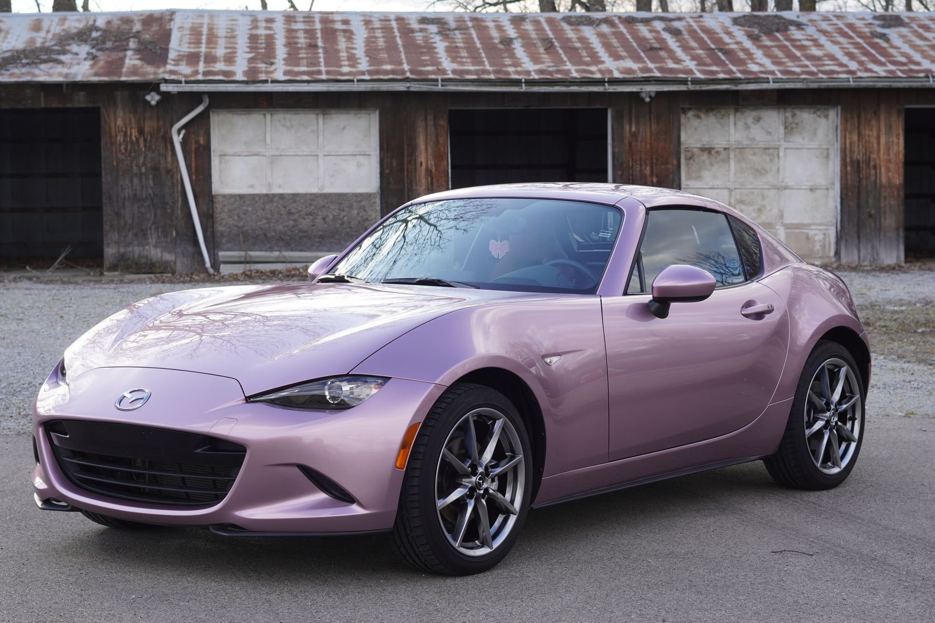 A pink Mazda MX-5 Miata sports car parked in front of a rustic wooden building.