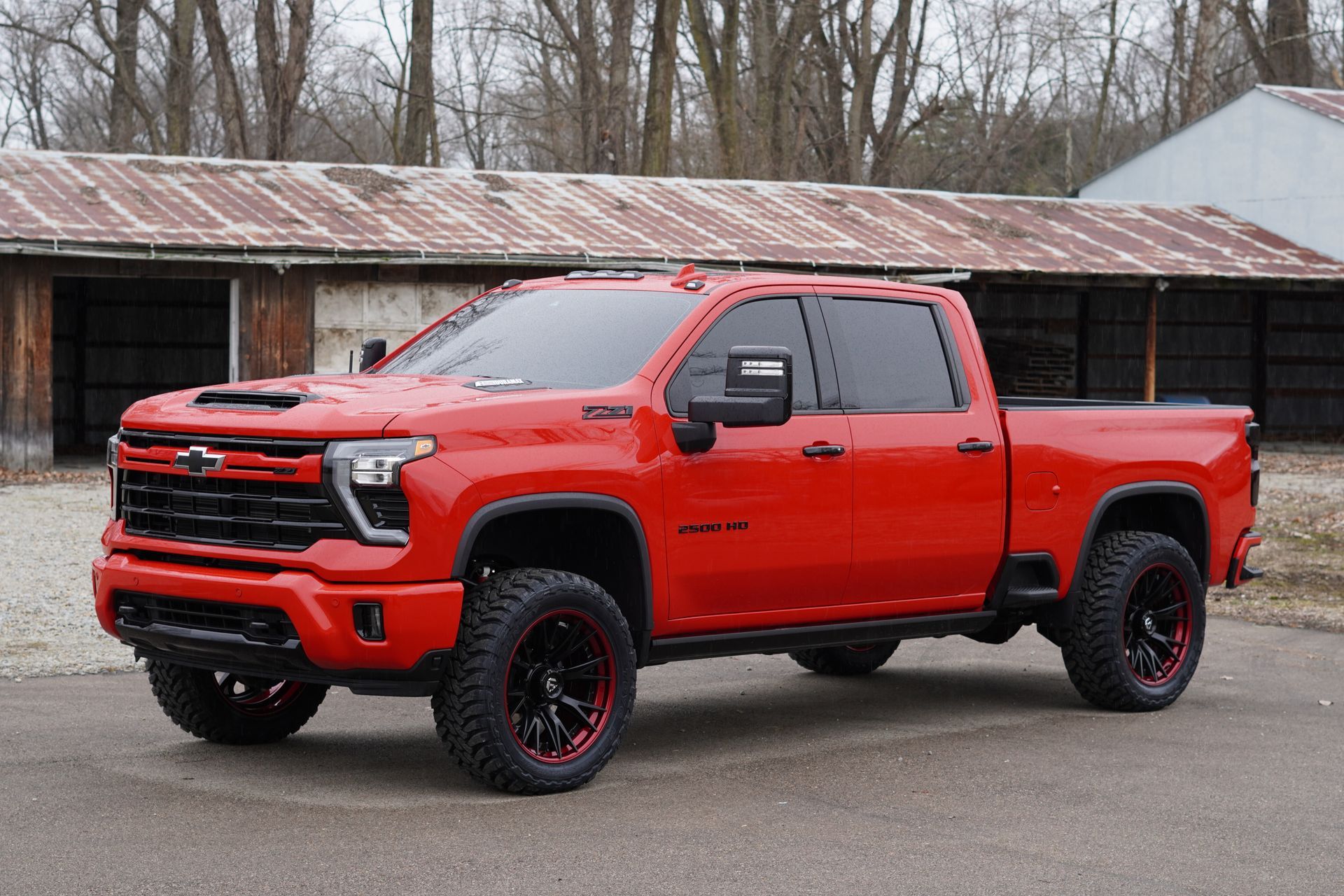 Bright red Chevrolet Silverado truck with black wheels parked in front of a weathered building.