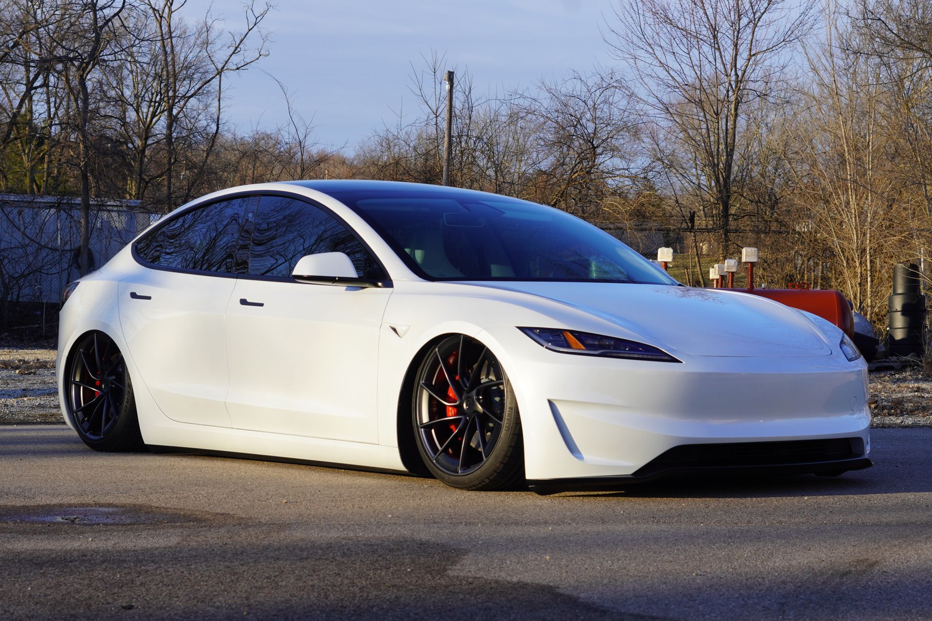 White Tesla sedan with black rims and lowered suspension, parked on a road.