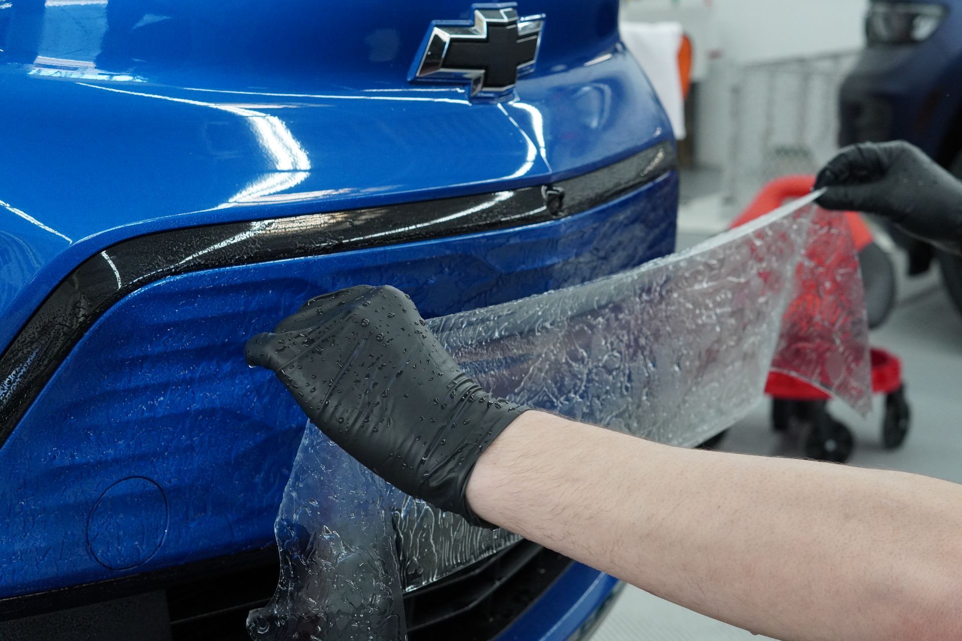 A person is wrapping the front bumper of a blue car.
