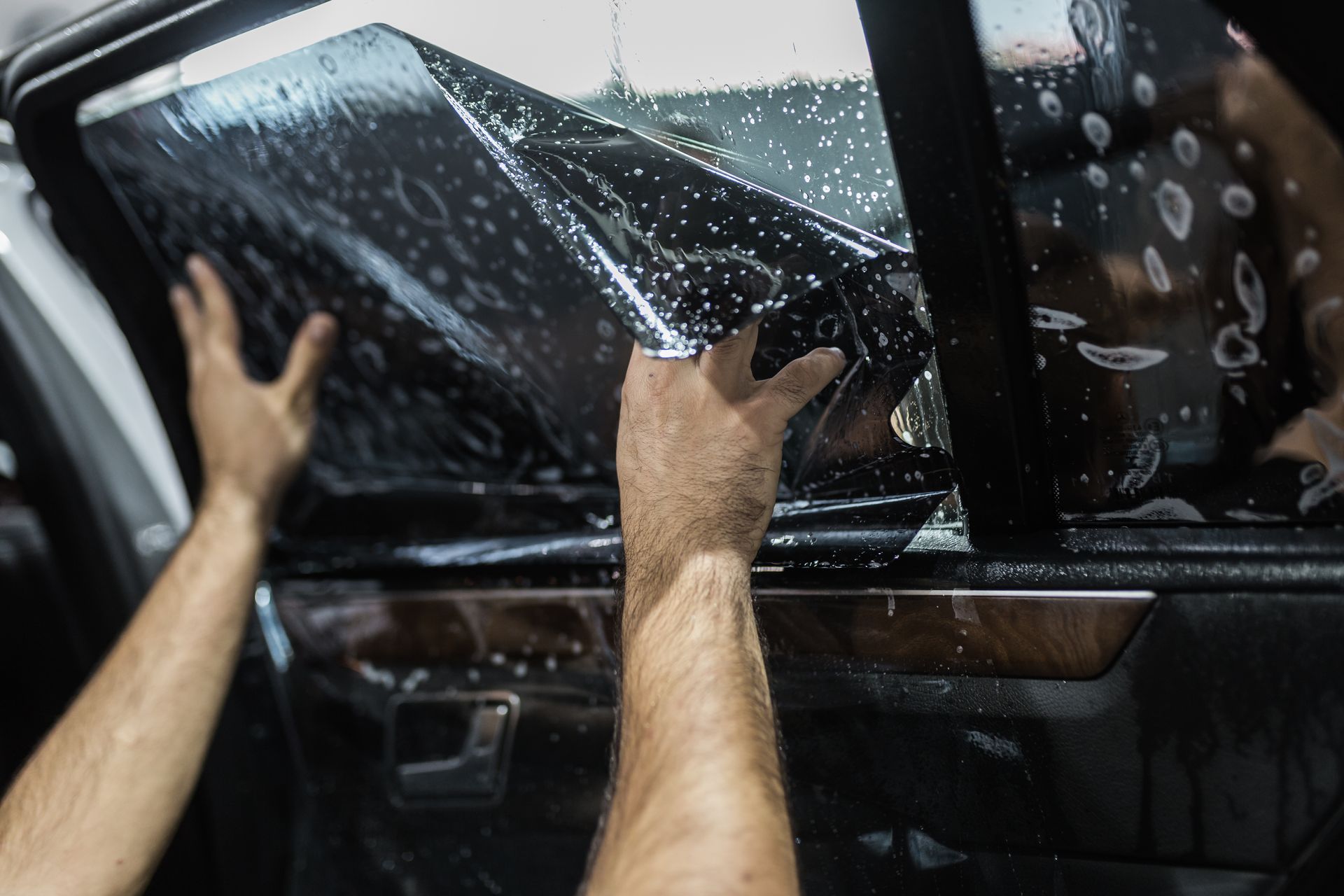 Hands cleaning a car window with soapy water in a car wash
