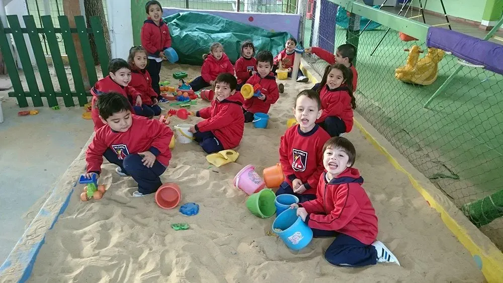 Niños vestidos de rojo jugando con juguetes coloridos en un arenero cercado.