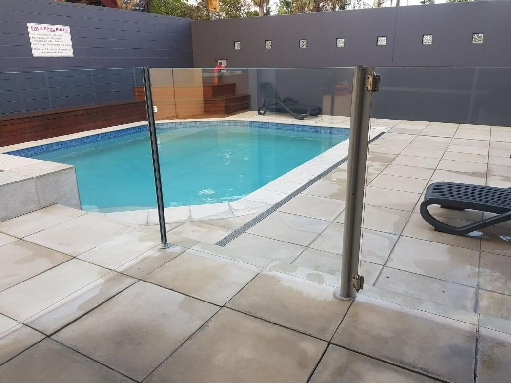 A Large Swimming Pool Surrounded By A Fence And Chairs Under An Umbrella — Scratchless Glass Australia in Maroochydore, QLD