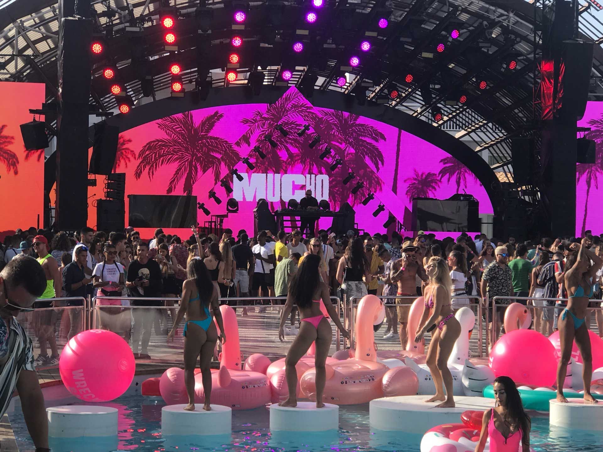 A crowd of people are standing in front of a stage that says mucho
