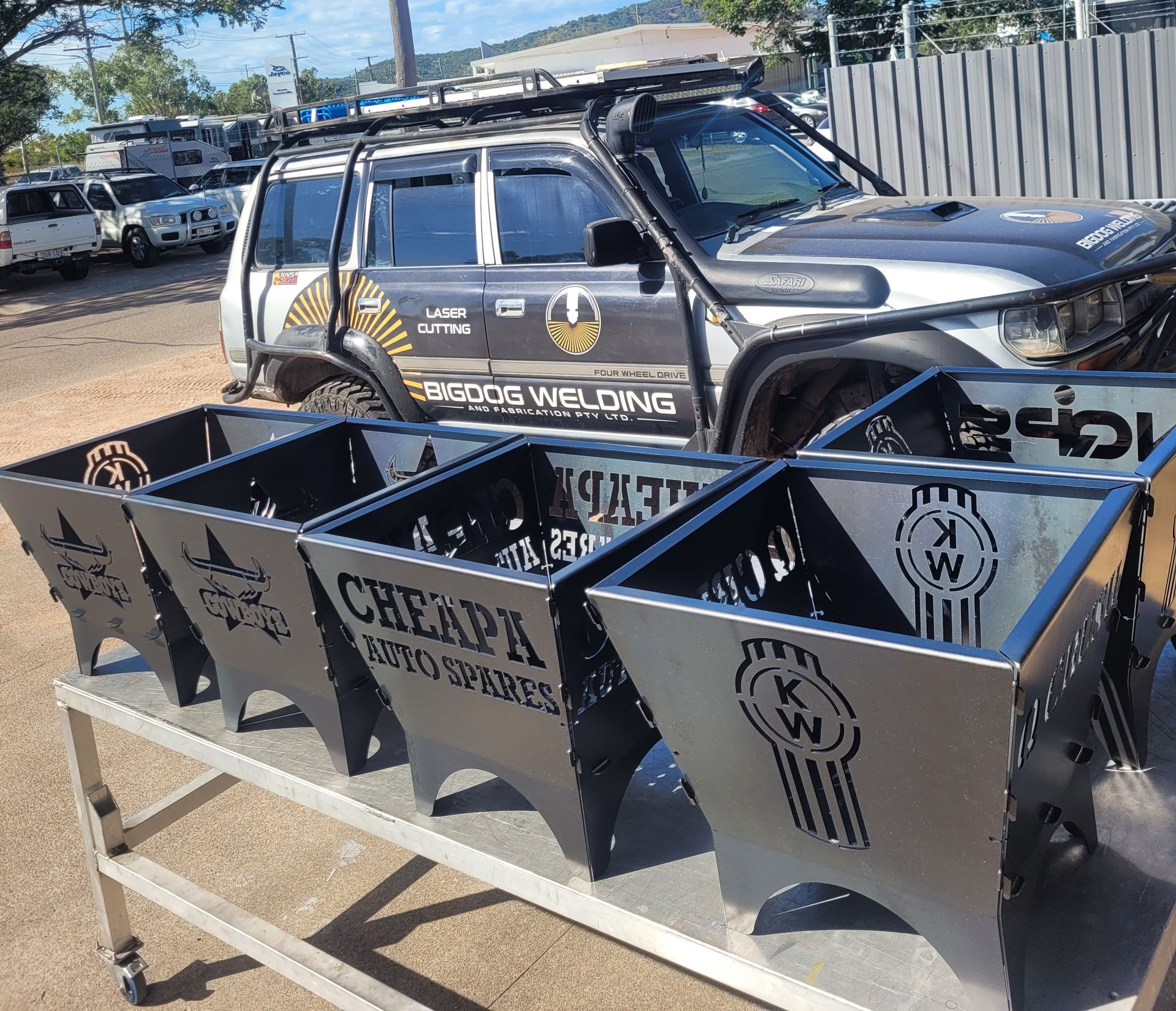 A Row Of Metal Fire Pits Are Sitting On A Table In Front Of A Car — Bigdog Welding and Fabrication Pty Ltd In Currajong, QLD