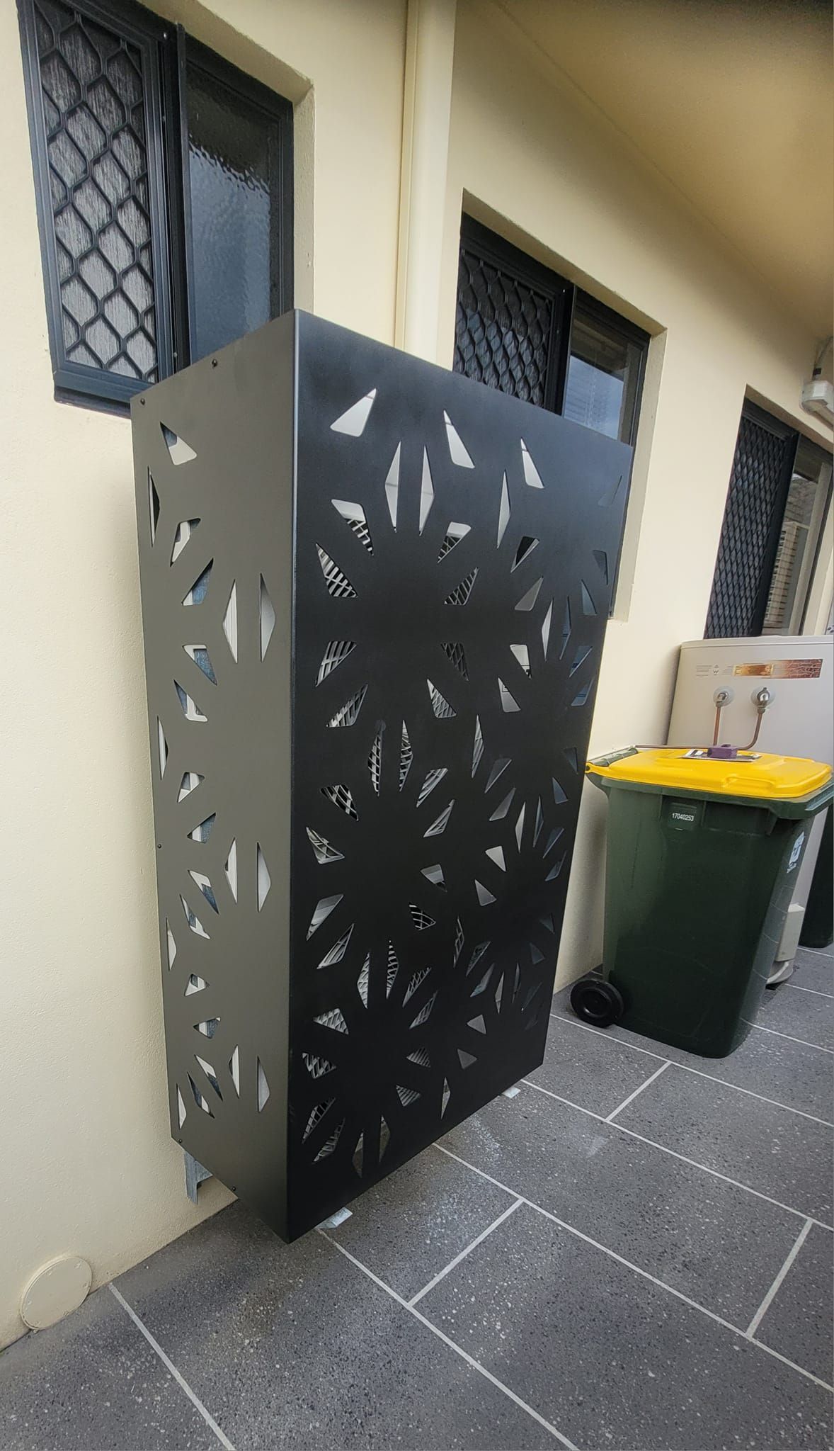 A Black Metal Fence Is Sitting On The Side Of A Building Next To A Trash Can — Bigdog Welding and Fabrication Pty Ltd In Currajong, QLD