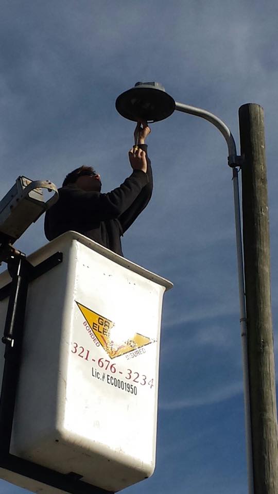 Utility worker in a bucket lift replacing a streetlight fixture on a pole