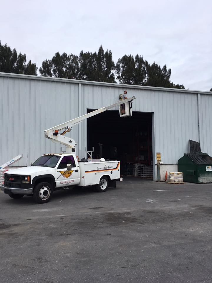 White utility truck with raised boom lift parked outside a warehouse loading bay.