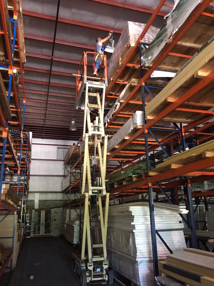 Warehouse interior with tall scissor lift reaching shelves, boxes stacked on racks and pallets below