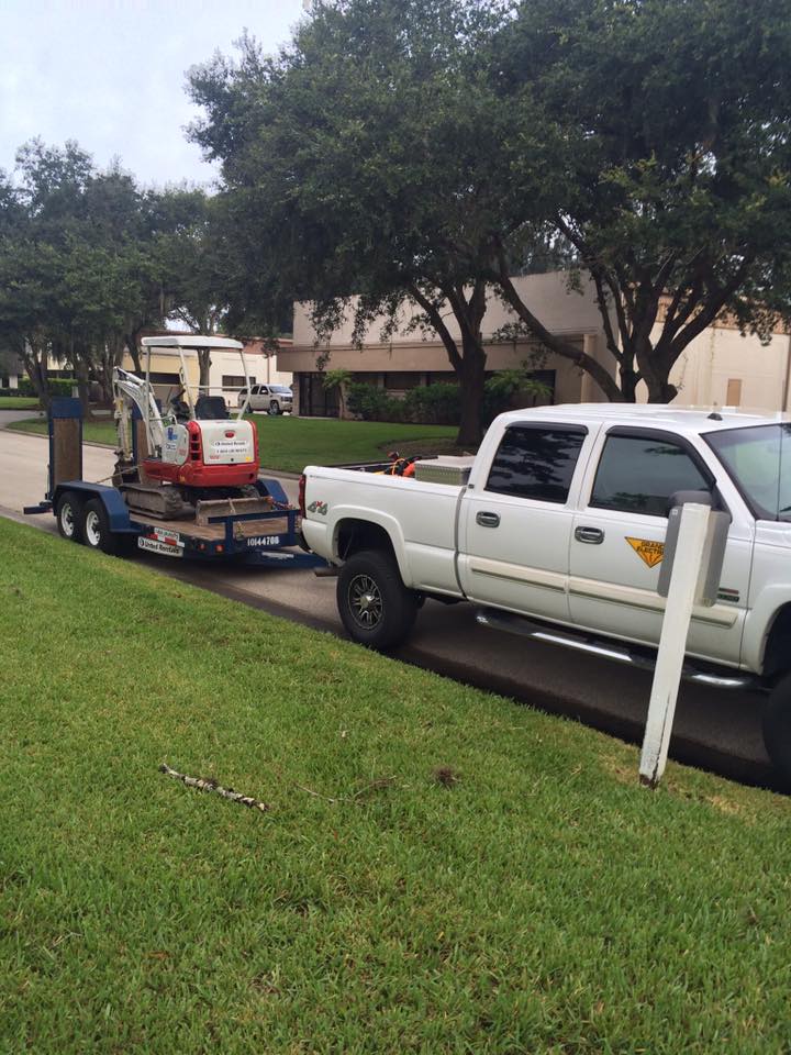White pickup truck towing a small red machine on a trailer along a suburban street.