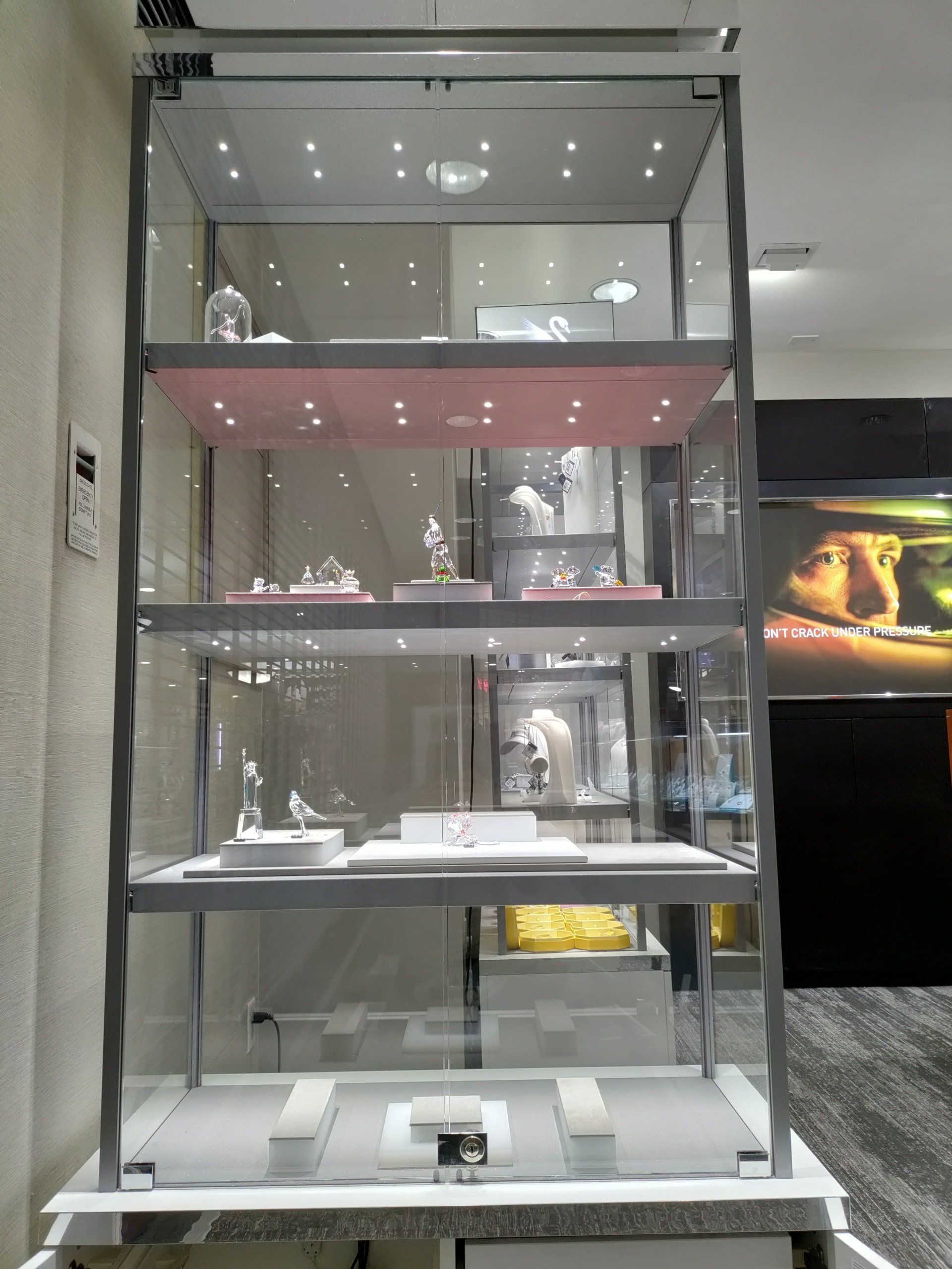 Glass display cabinet with shelves of small white objects and lights inside, in a showroom.