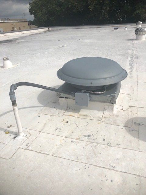 Gray rooftop ventilation unit with a curved hose on a white flat roof under cloudy sky
