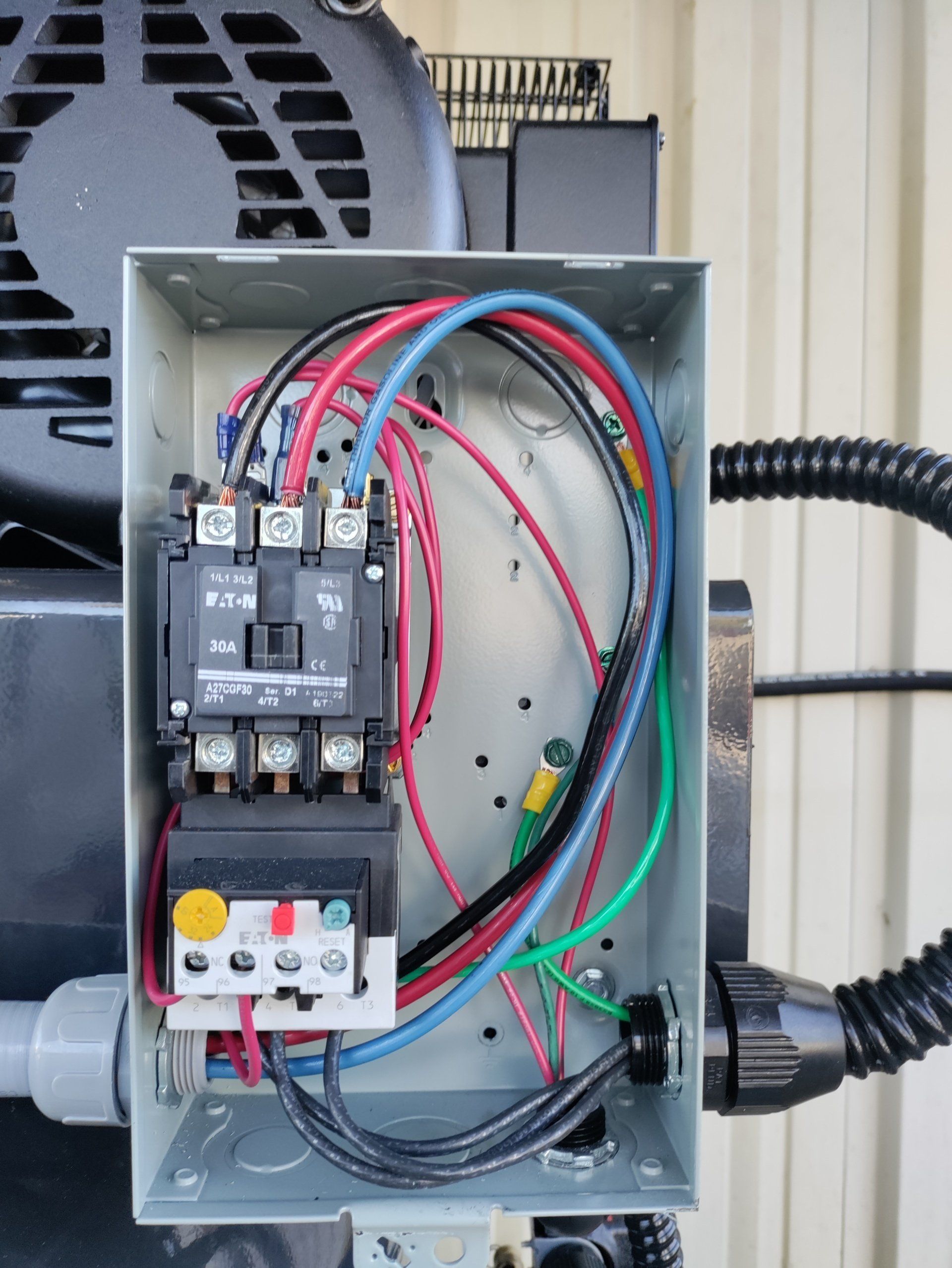 Open electrical control box with wiring, relays, and circuit breaker mounted beside equipment.