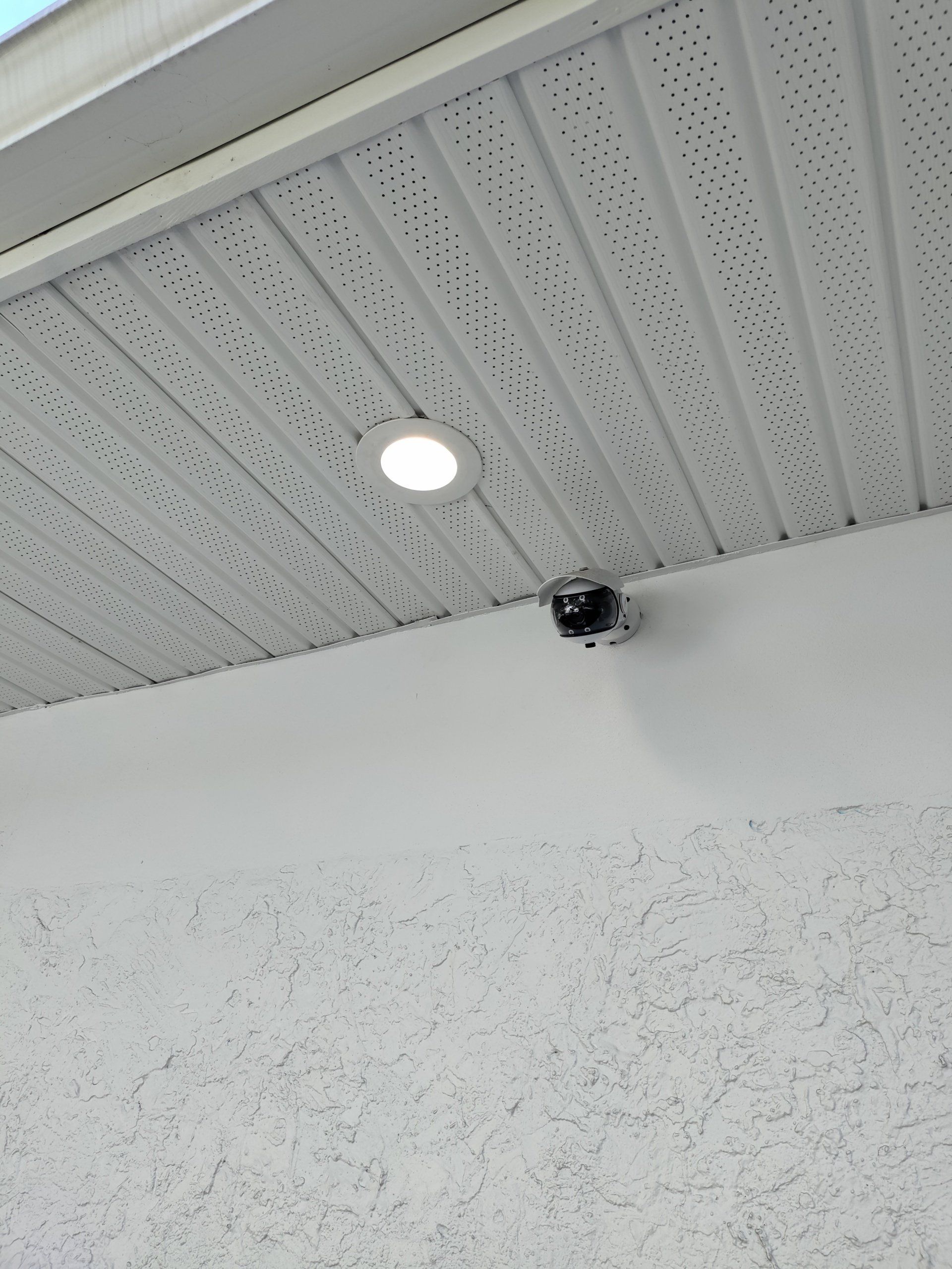 Ceiling with recessed light and a small dome security camera above a speckled wall