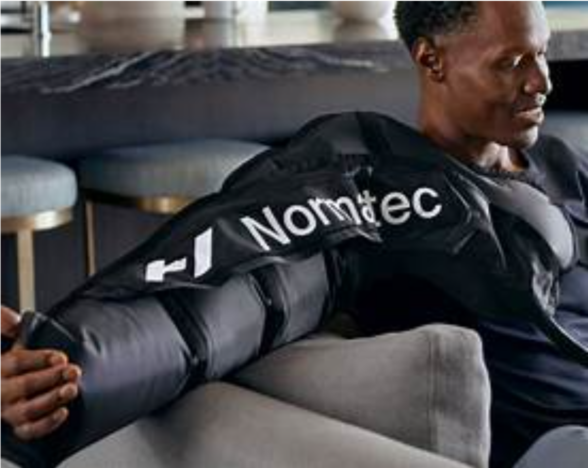 Man wearing a black Normatec leg compression sleeve while reclining on a couch