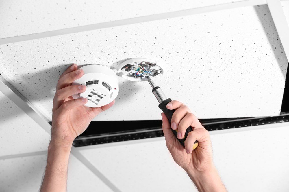 A Person is Installing a Smoke Detector on the Ceiling — Brightway Electrical in Ballina, NSW