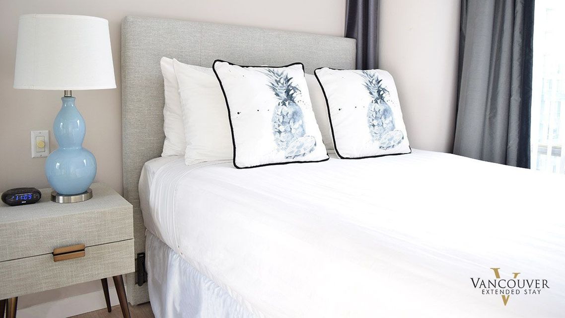 Two white pillows with a blue pineapple design on a twin size bed next to a baby blue lamp