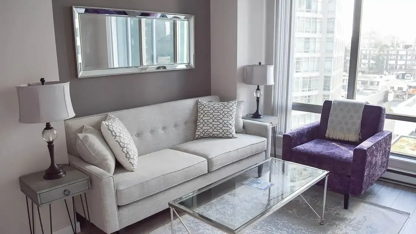Two sofa pillows with line designs on top of a sofa next to a glass coffee table and a mirror