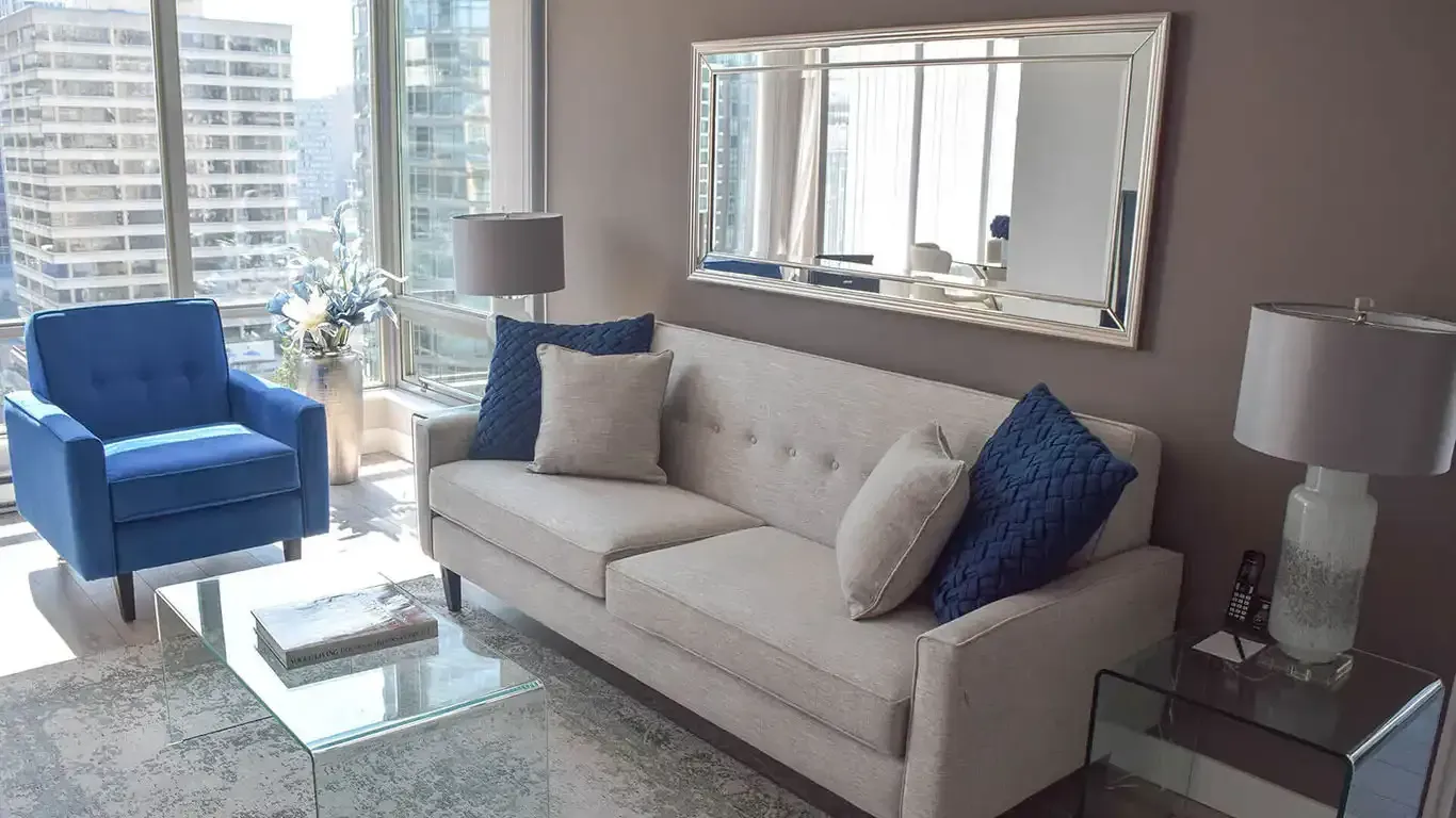 two plain grey sofa pillows and two blue plain sofa pillows on a grey sofa next to a glass coffee table and a mirror