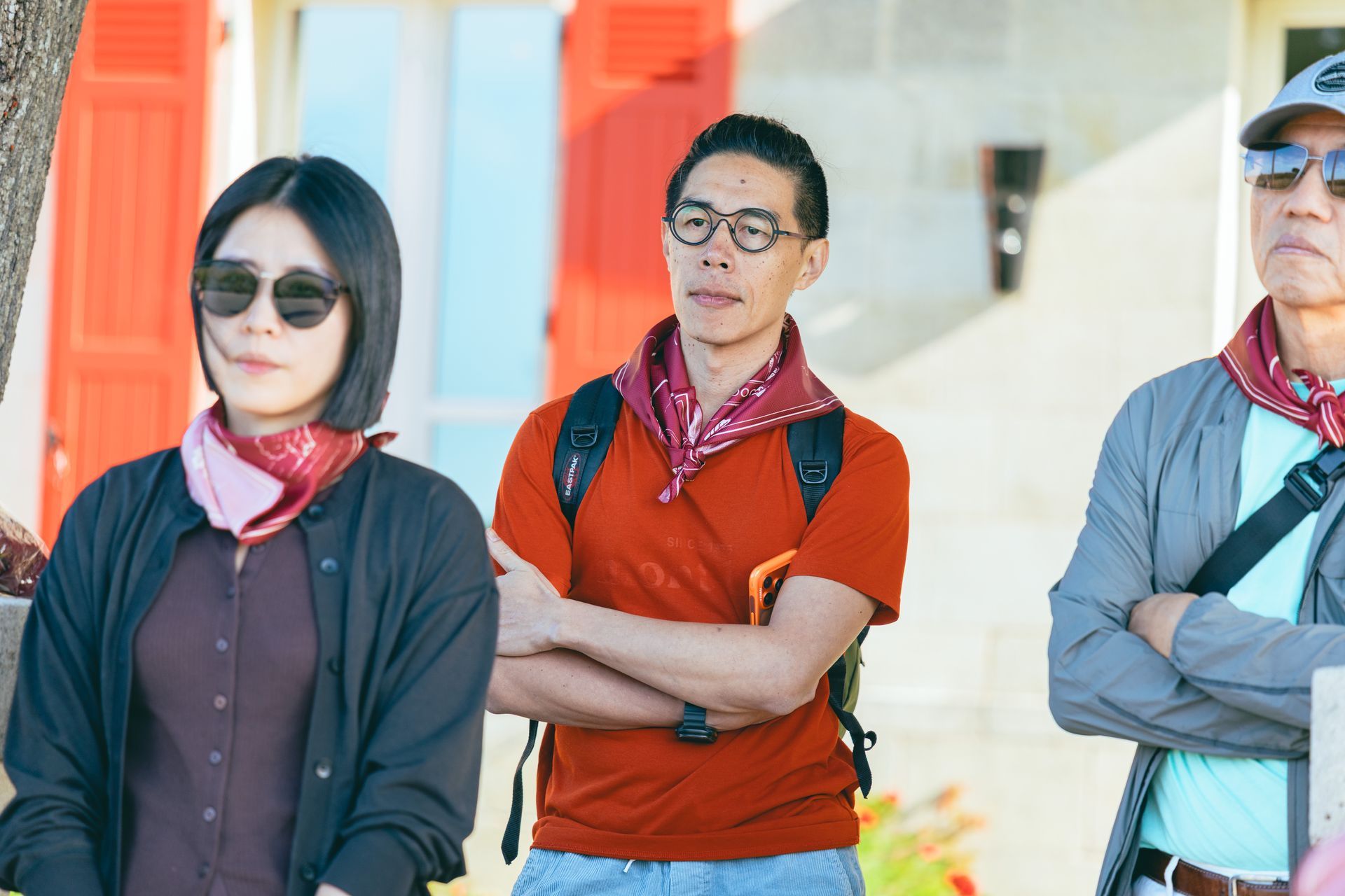 三個人站在室內,戴著太陽眼鏡和圍巾,雙臂交叉。