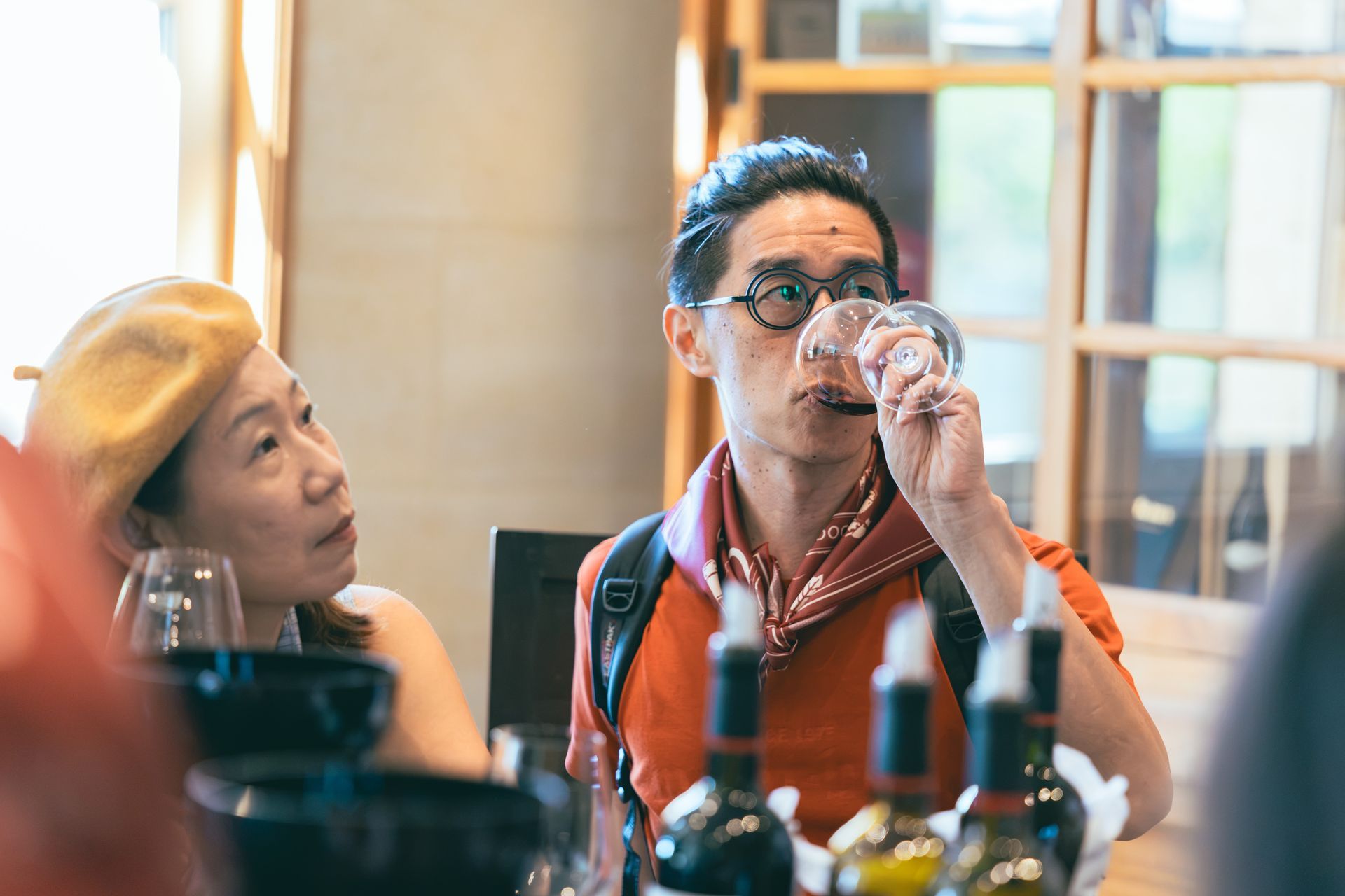 兩人在餐廳桌旁品酒,前景擺著酒瓶和酒杯。
