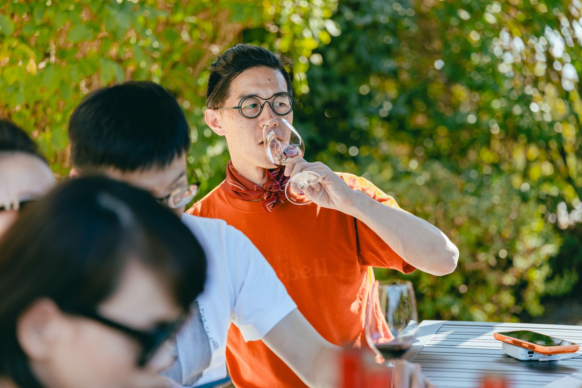 一名穿著橘色上衣的男子在聚會期間於戶外餐桌旁用餐