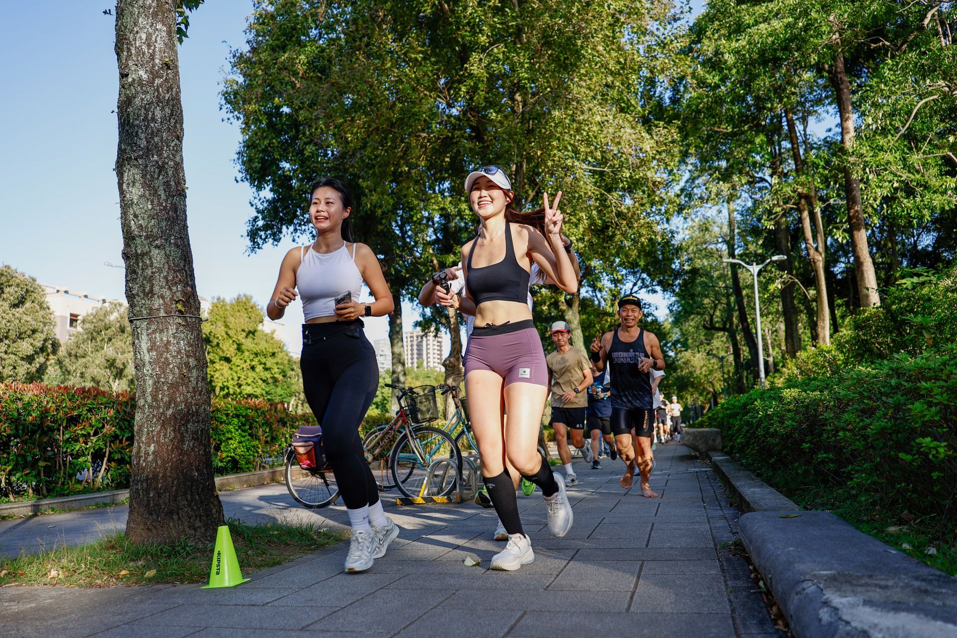 陽光明媚的日子裡，人們在兩旁綠樹成蔭的公園步道上慢跑。