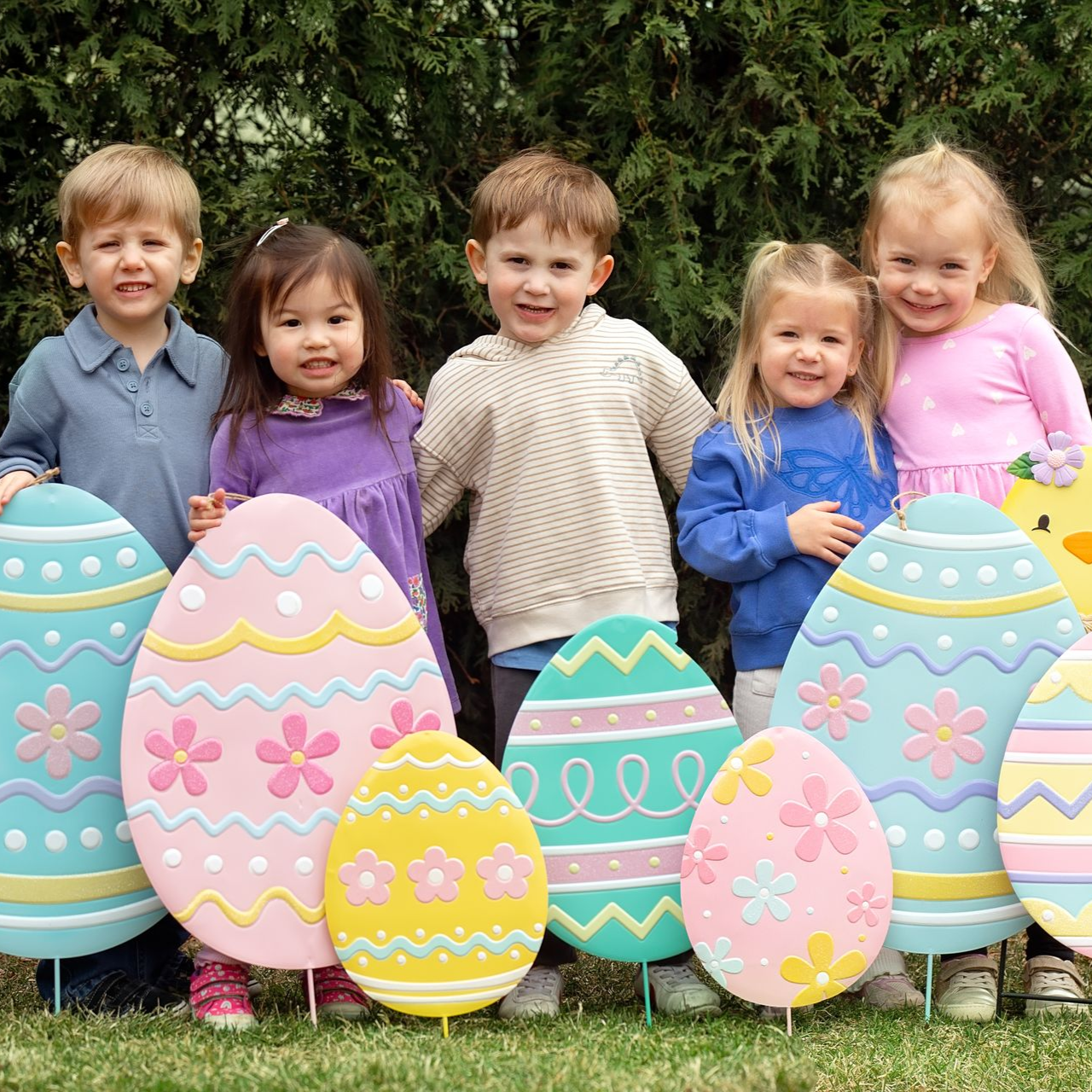 Children standing behind colorful painted Easter eggs outdoors